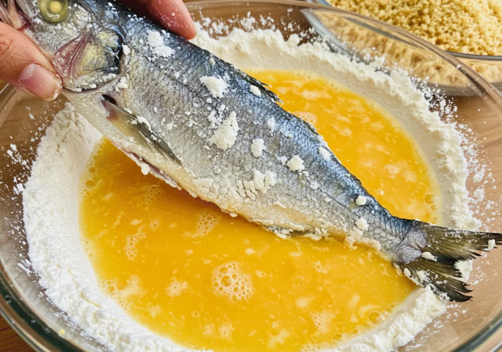 Mergulhando agulhinha peixe em ovo batido para o preparo de frito crocante.