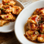Golden-brown honey pepper chicken pieces glistening with sticky sweet spicy glaze, served on a white ceramic plate with sesame seeds sprinkled on top, alongside steamed broccoli and jasmine rice in a ramekin. Soft natural daylight highlights caramelized edges and glossy texture.